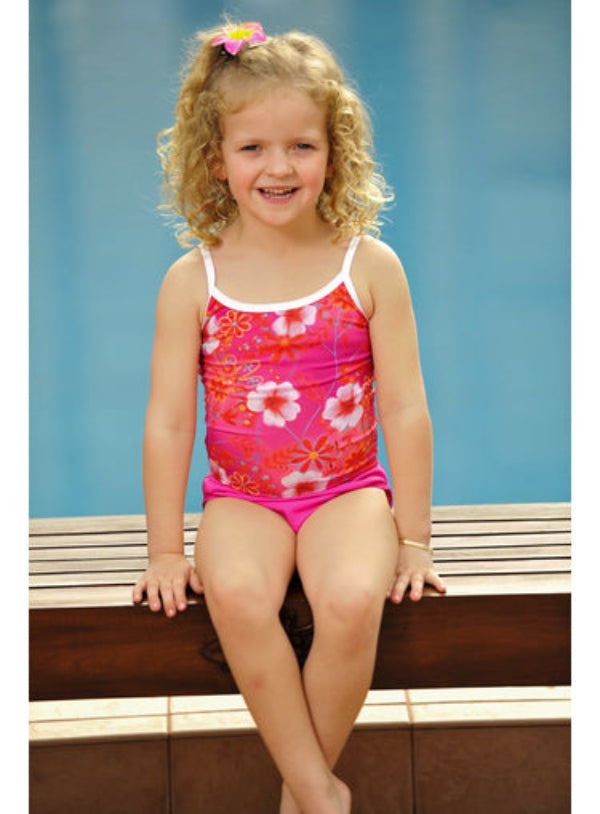 A young girl sitting by a poolside wearing a pink and red floral print tankini top.