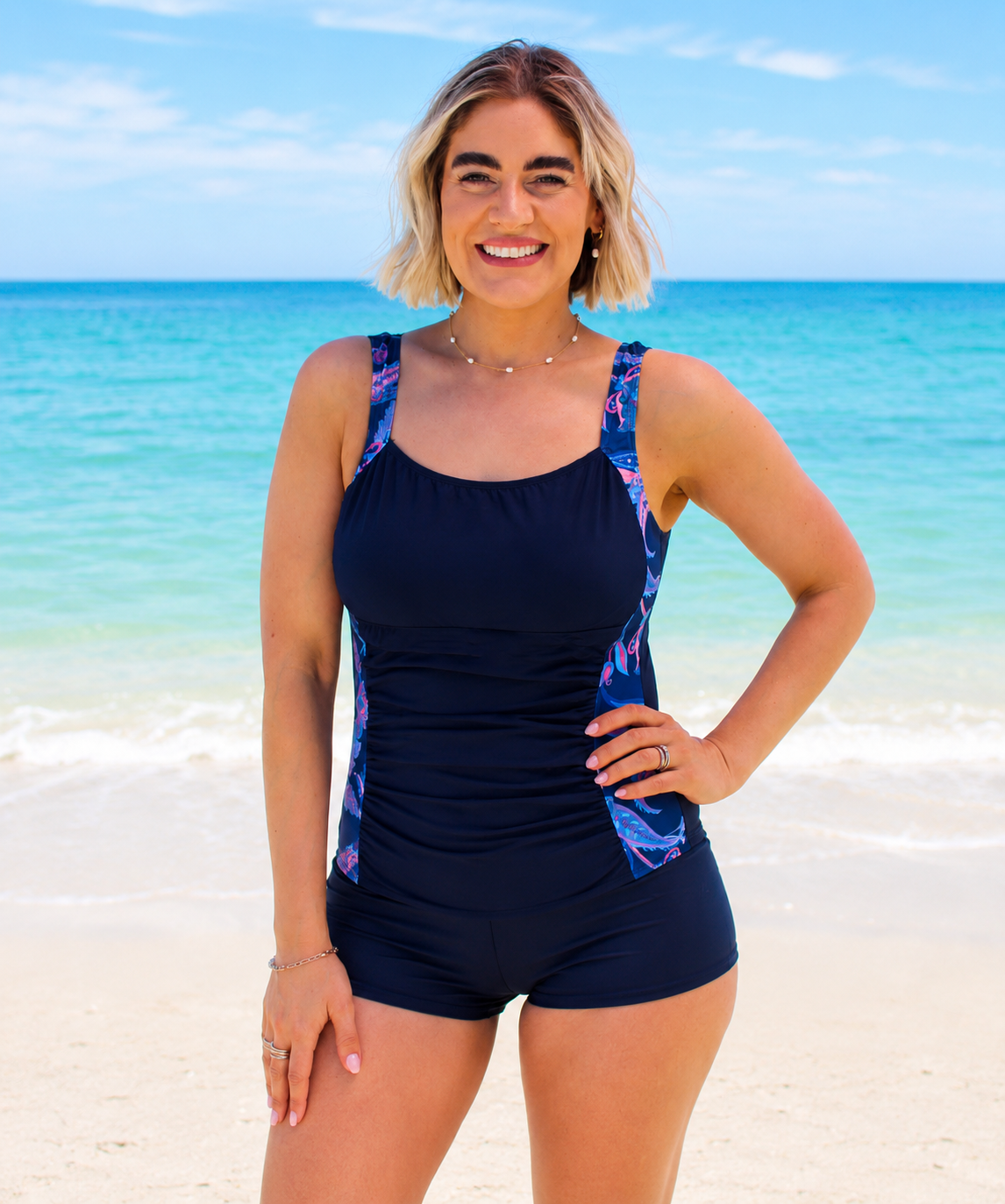 Woman wearing a black swimsuit with colorful floral side panels on a beach.