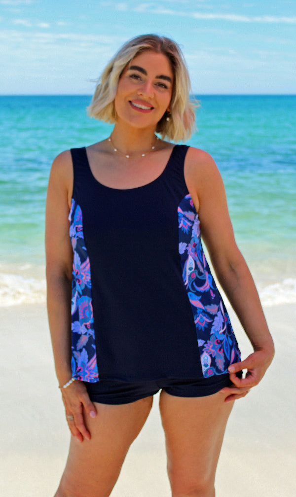 Woman wearing a navy tankini with colorful side panels on a beach.