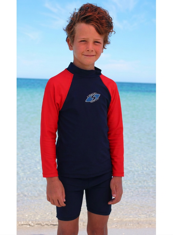 Boy wearing a red and navy long sleeve rash with a logo on a beach